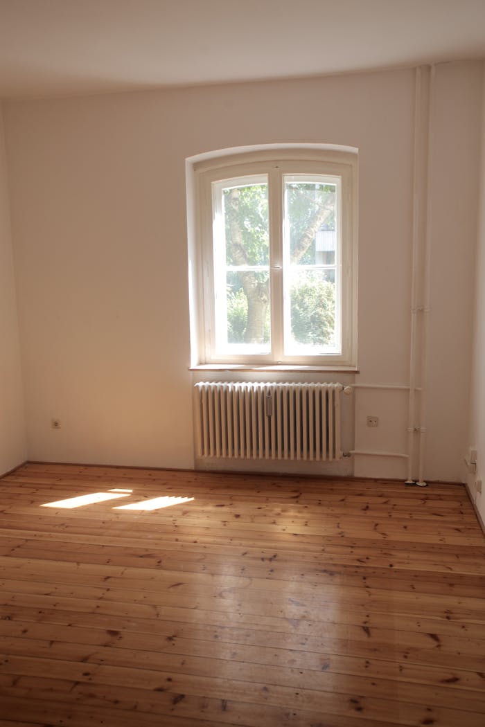 Spacious empty room with wooden floor and large window in Berlin, ideal for interior planning.